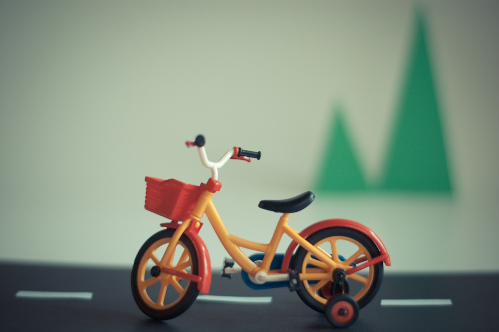 A tiny plastic toy bike sits on a simple vinyl road, ready for a toy rider to take over the toy world.