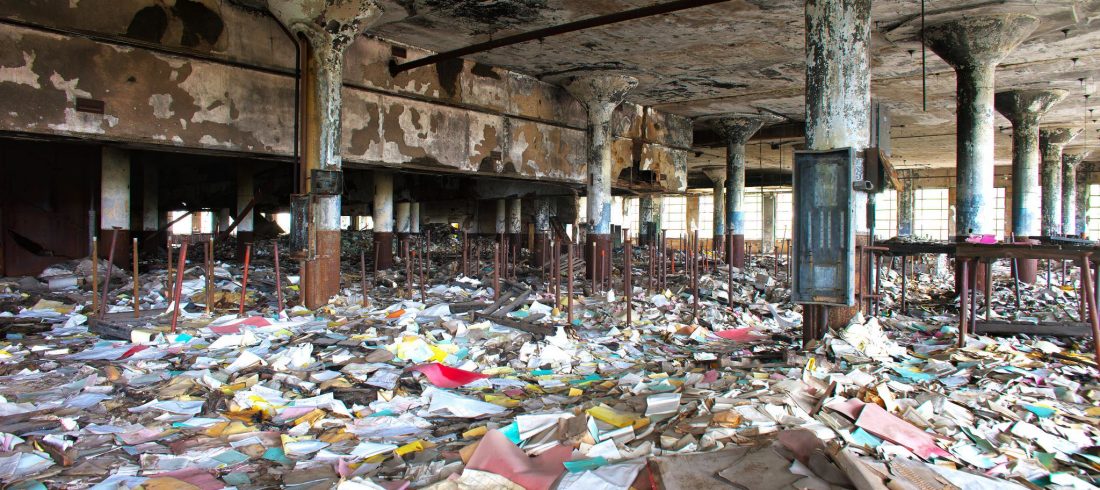Abandoned warehouse, floor covered with books and papers strewn all around.