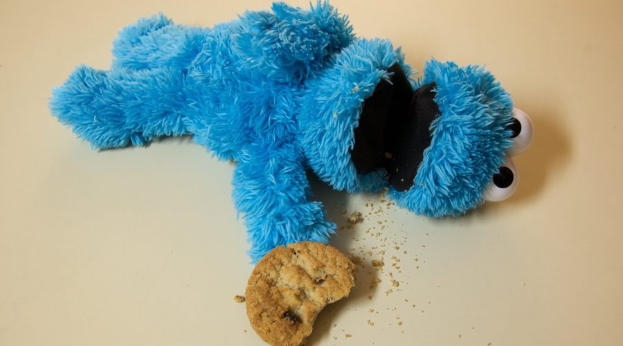 plush Cookie Monster lying on its back, apparently dead, cookie with one bite taken out left at tip of outstretched hand