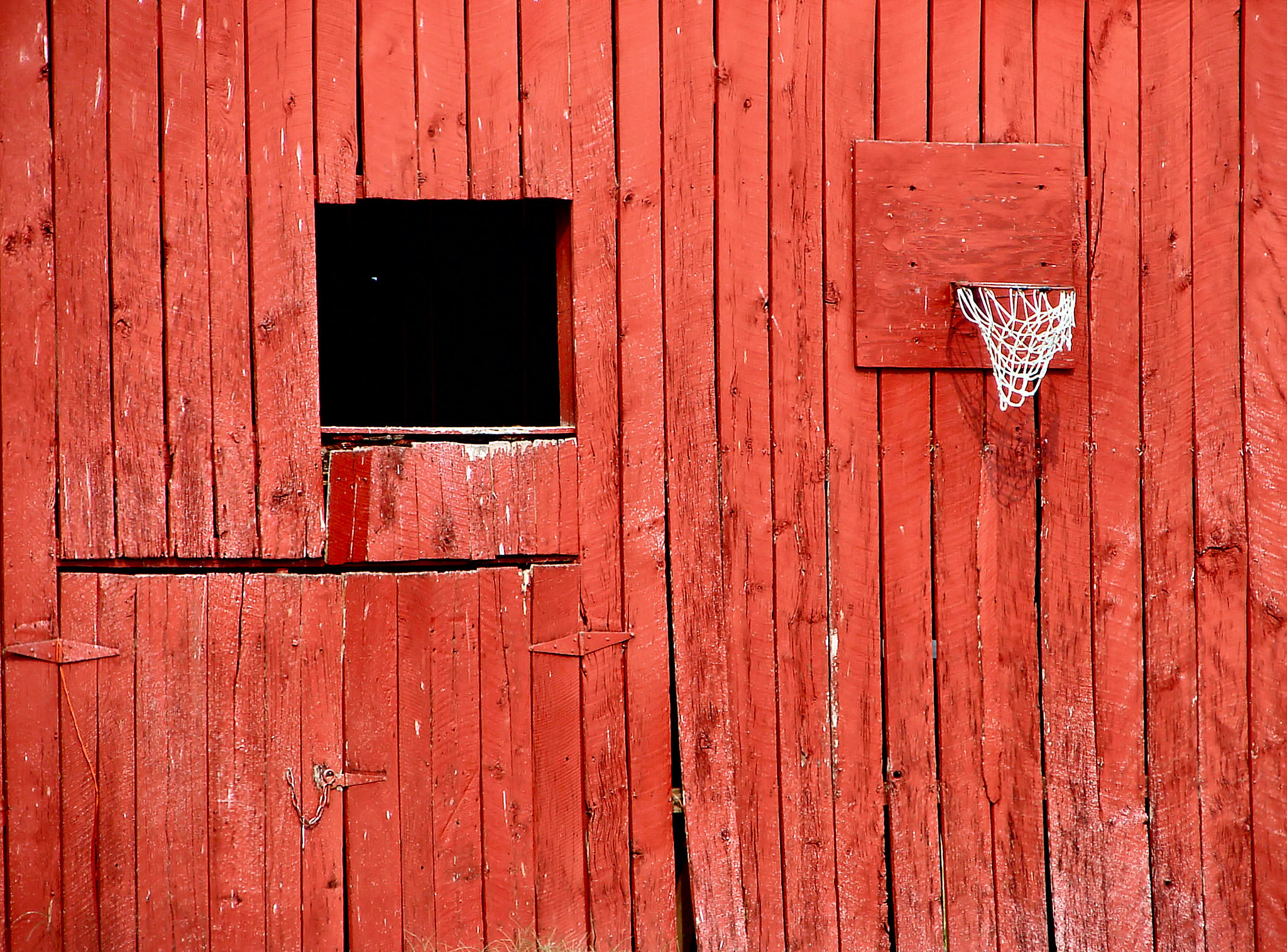 A red-painted wooden wall, likely the side of a barn. What's inside that gap?