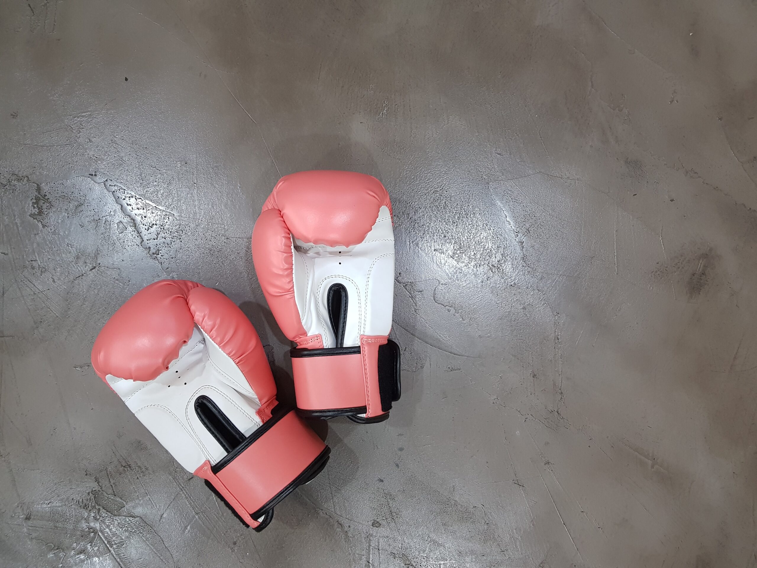 a pair of pink and white boxing gloves lie on a concrete surface