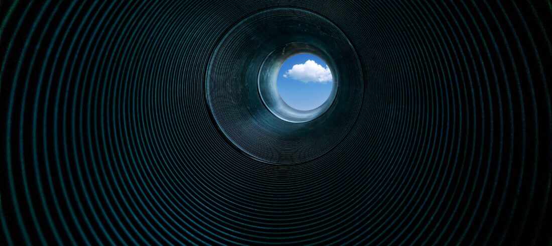 looking through a corrugated metal pipe toward a rich blue sky with white cloud in center of view