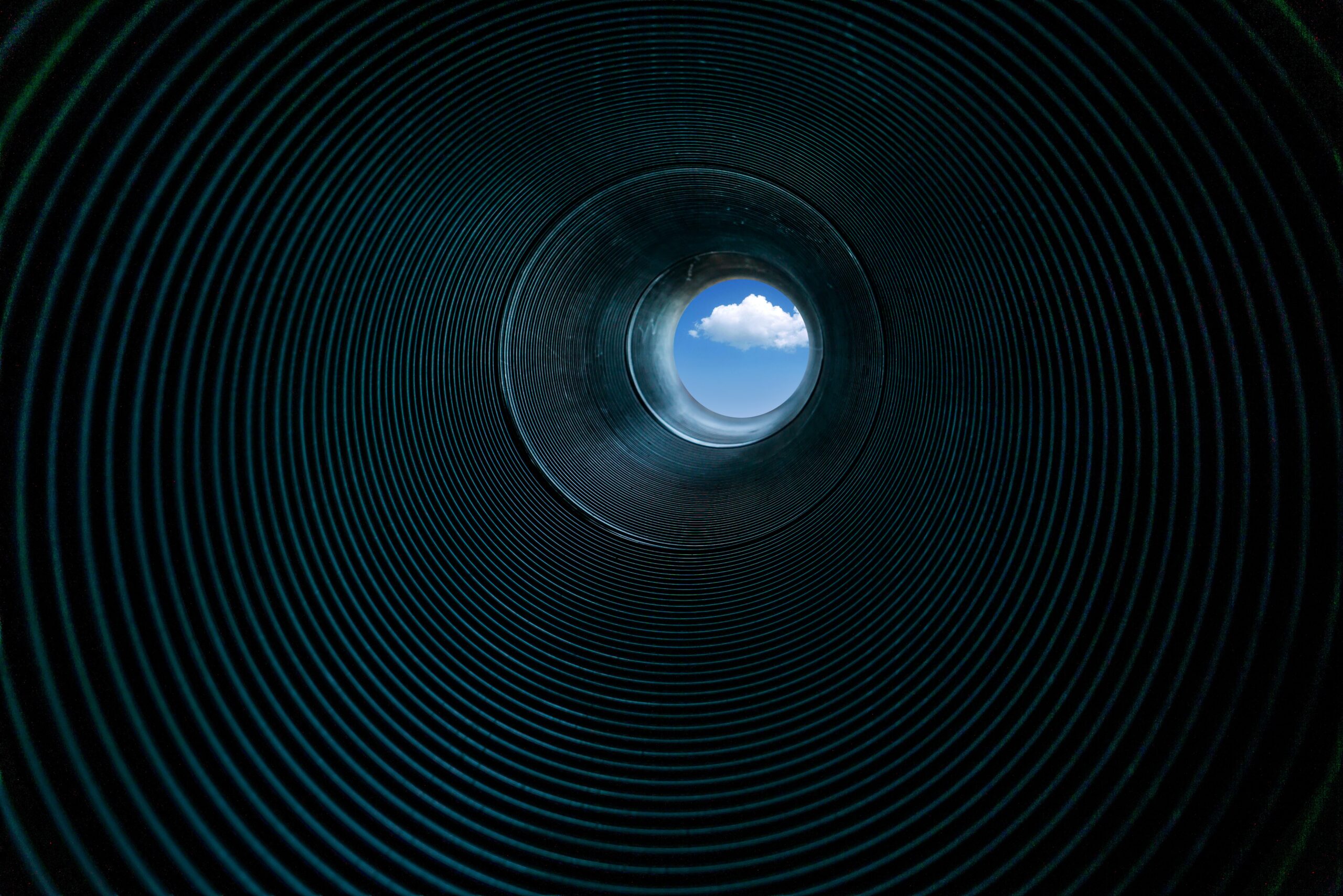looking through a corrugated metal pipe toward a rich blue sky with white cloud in center of view