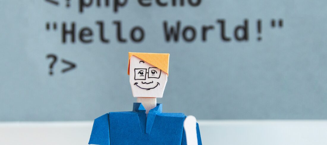 paper figure of blond-haired white person in collared shirt and glasses waves at camera in front of "Hello world" echo statement written in PHP