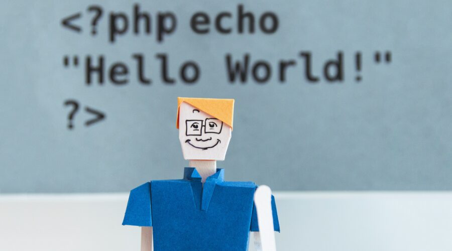 paper figure of blond-haired white person in collared shirt and glasses waves at camera in front of "Hello world" echo statement written in PHP