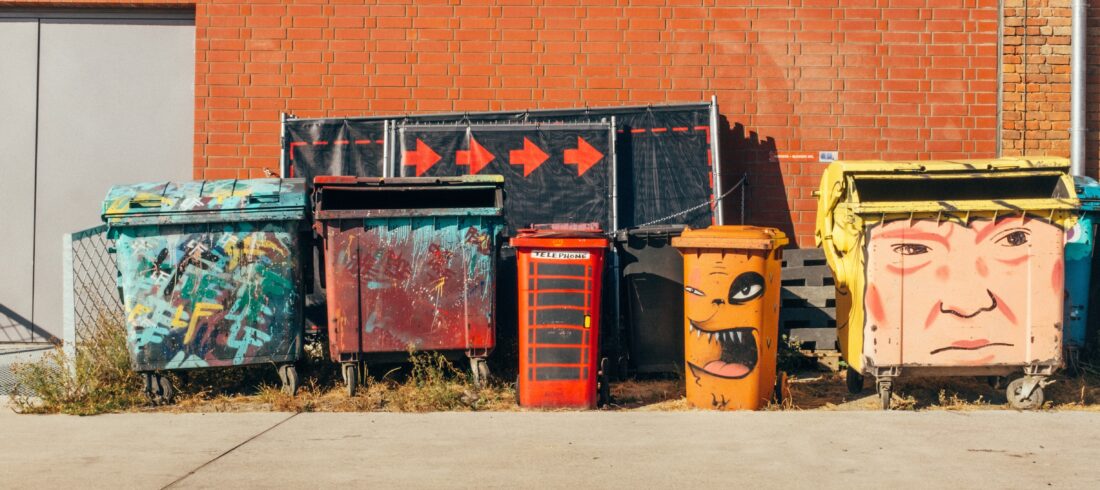 A collection of colorful, art-covered dumpsters and trash bins. They are the medium; what message to they convey?